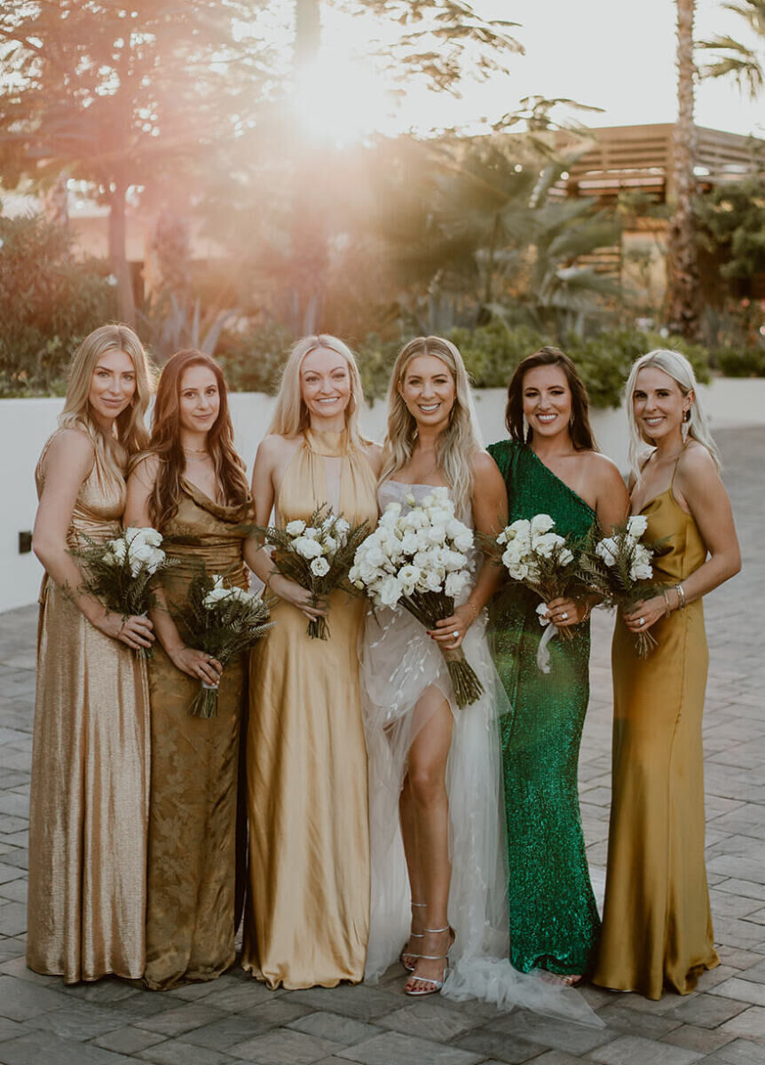 A bride, surrounded by her bridesmaids who wore long gowns in shades of gold and green, and carried white bouquets.