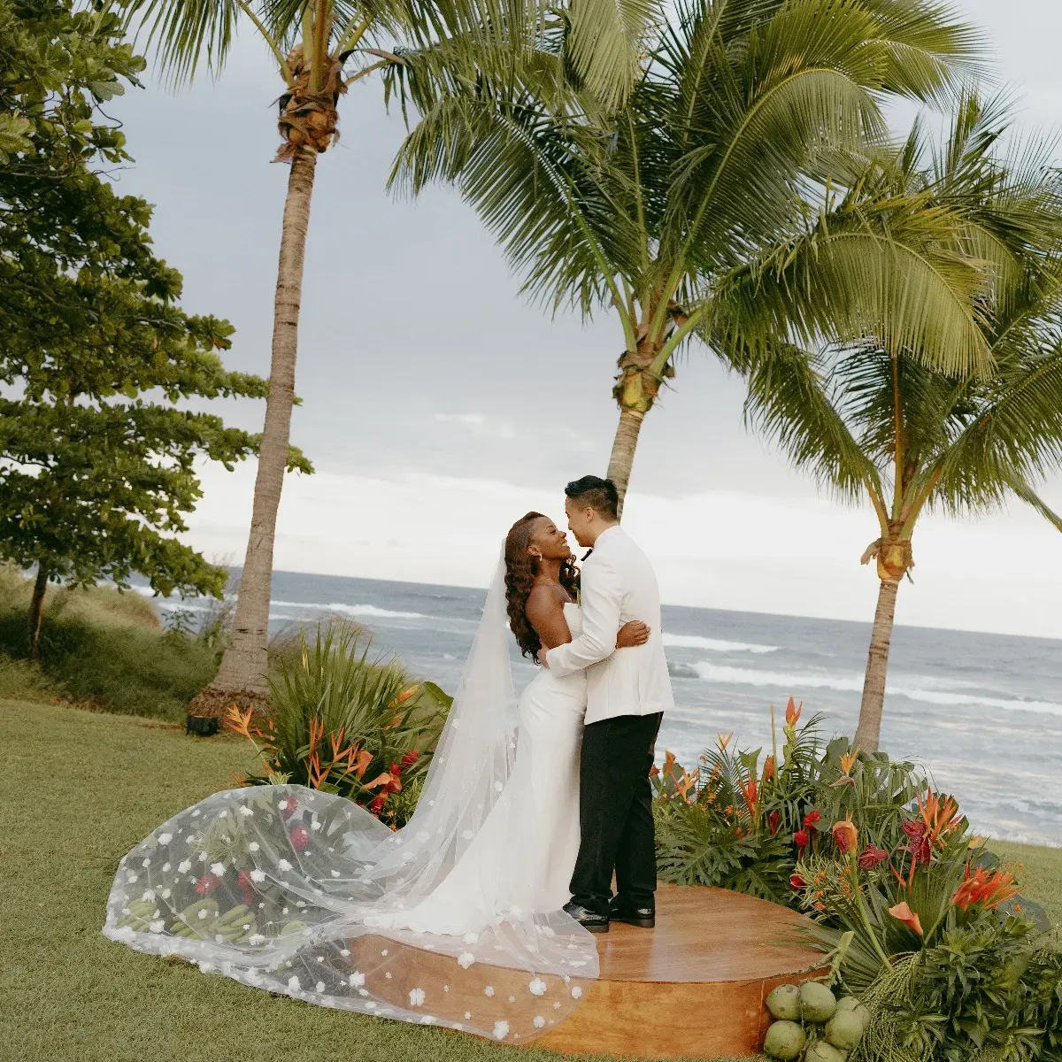 A wedding couple embracing on a Costa Rica resort's lawn with palm trees and the ocean in the background, photographed by Kuba Okon Weddings
