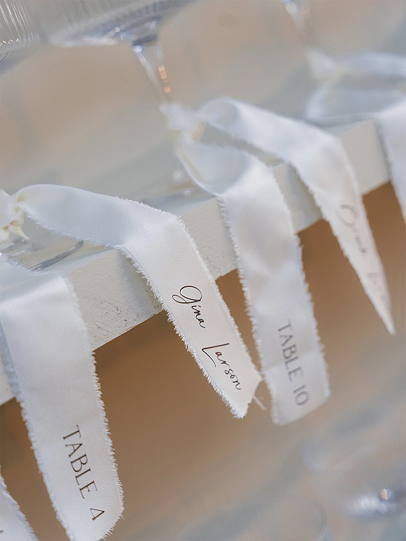 Wedding place cards with calligraphy place cards tied in torn edge ribbon, paired with table numbers and glassware on a neutral table setting