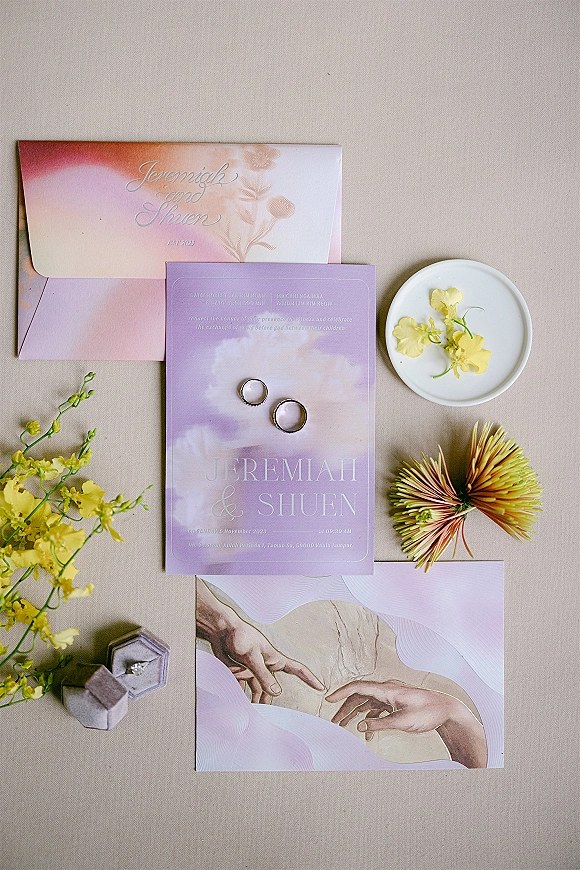 Wedding invitation suite with pastel wedding invitations, rings and engagement ring in a box, styled with flowers on a linen backdrop
