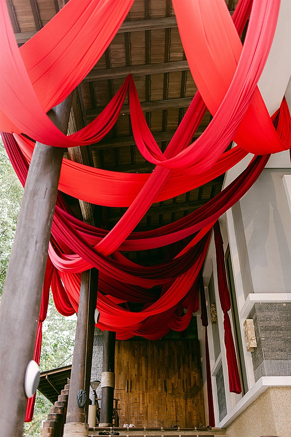 Ceiling drape decor with red ceiling draping crisscrossed into fabric swags, tied to wood beams along a staircase walkway