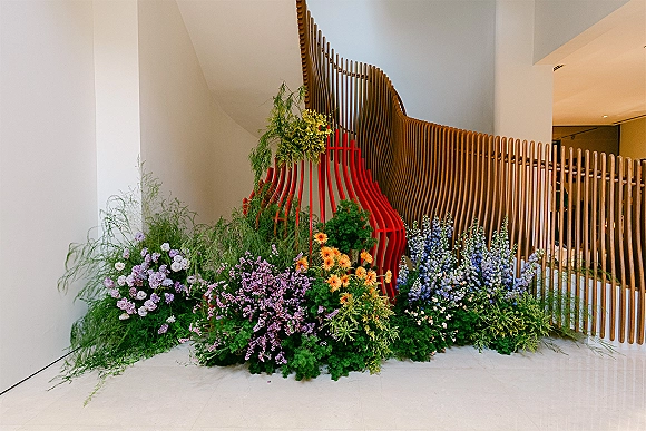 Wedding floral installation with lush greenery and colorful blooms cascading along a modern staircase, set against a red sculptural backdrop