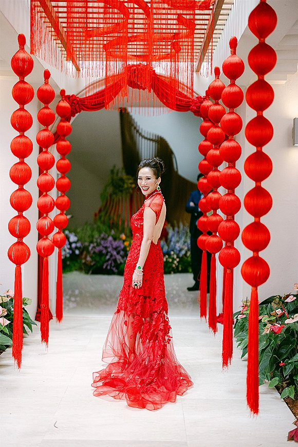 Bridal portrait in a red wedding dress with lace and sheer tulle train, framed by red lantern garlands in a white hallway