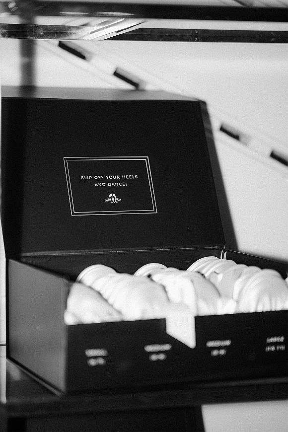 Wedding favor box with flip flop wedding favors label, black gift box tied with ribbon beside flip flops on stacked tabletop display