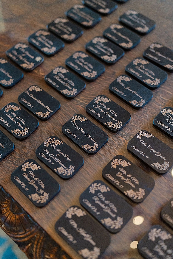 Wedding place cards in black with white calligraphy and floral corner motifs arranged neatly on a rustic wood table