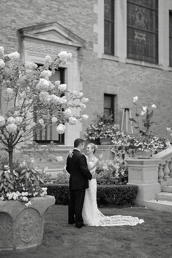 Couple portrait of bride and groom embrace on stone steps outside a brick church with stained glass windows, her train flowing behind