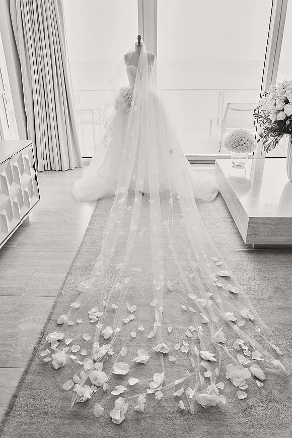 Wedding dress displayed on a mannequin, strapless gown with long bridal veil draped over rose petals by floor-to-ceiling windows