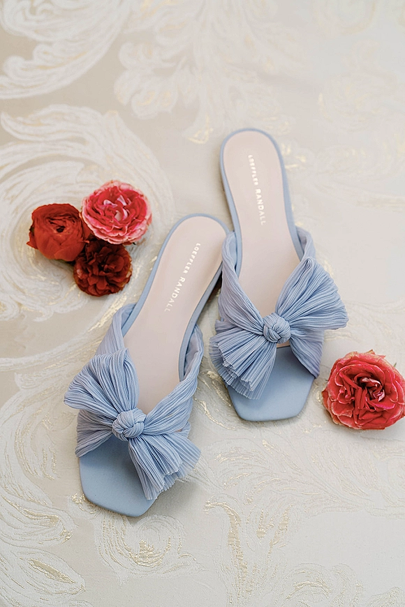 Bridal shoes, something blue shoes with pleated light blue bow mules and flowers arranged on a patterned neutral fabric surface
