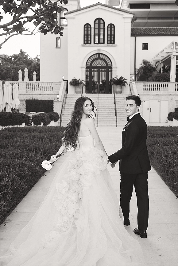 Couple portrait in a black and white wedding portrait, bride and groom holding hands on a grand staircase, her long train flowing behind
