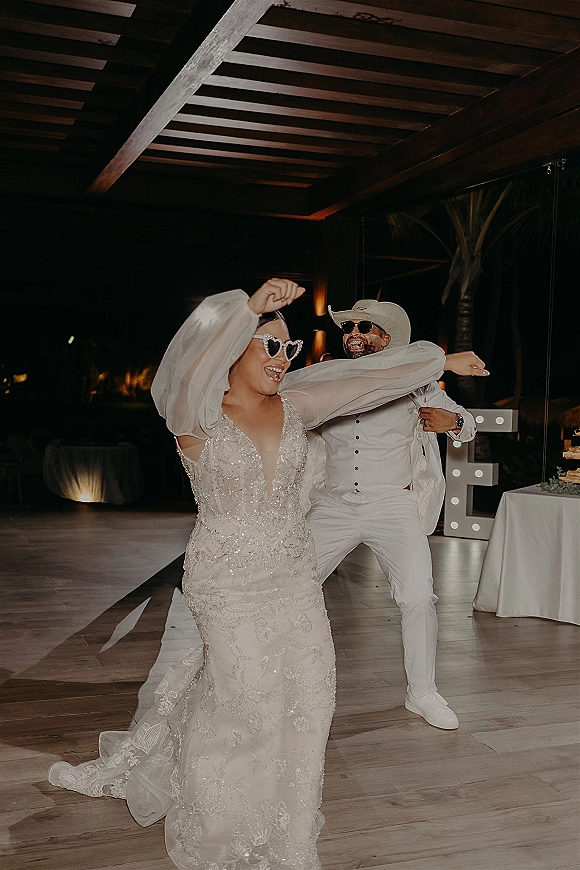 Wedding reception dancing as the bride and groom dance in heart sunglasses, with groom in a cowboy hat beside light-up marquee letters indoors