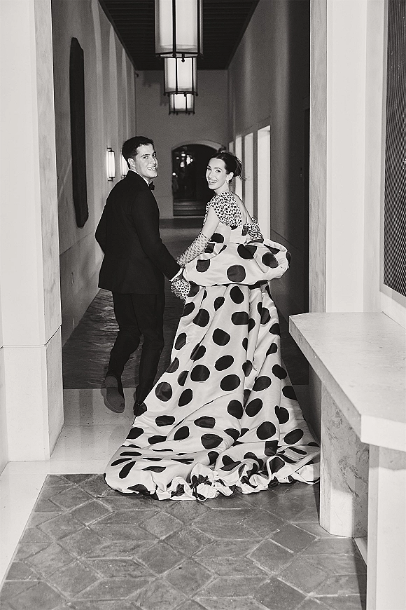 Couple portrait in a lantern-lit hallway, bride in polka dot wedding dress with long train and gloves, holding hands as they look back