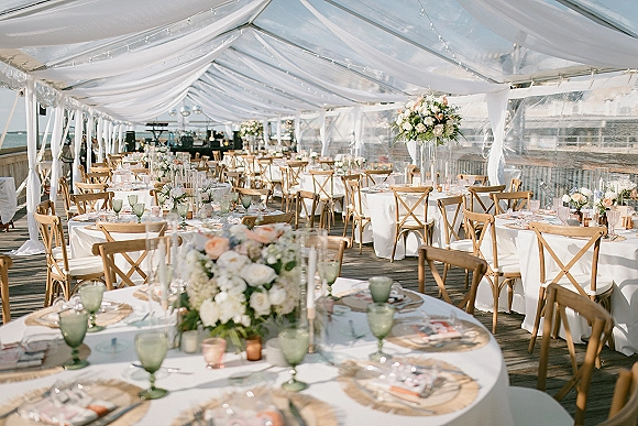 Reception tablescape at outdoor tented reception with white linens, green goblets, floral centerpieces and candles under string lights by the ocean
