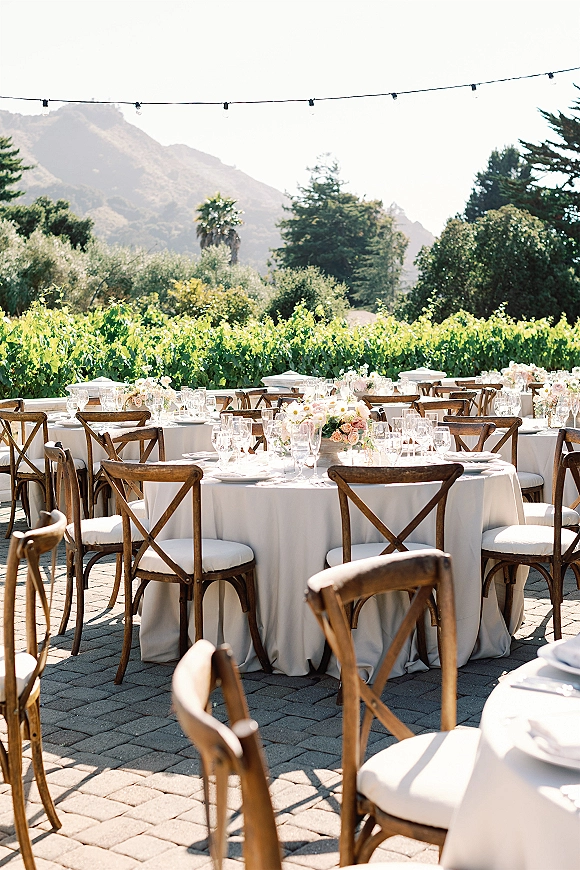 Reception tablescape for an outdoor wedding reception with round tables, white linens, blush centerpieces, glassware, string lights, mountains beyond