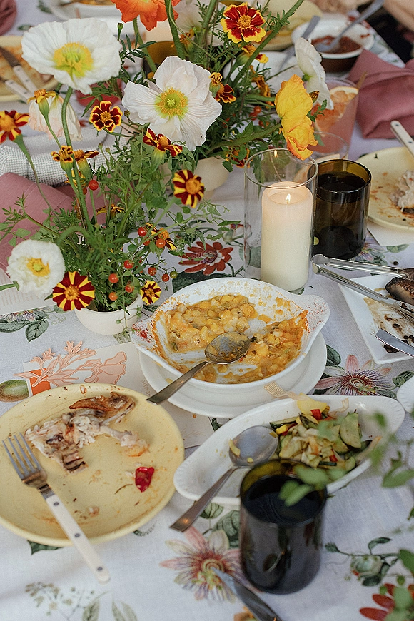 Wedding tablescape with wildflower wedding centerpieces of poppies and marigolds, pillar candle in hurricane glass, guest hands at dinner table