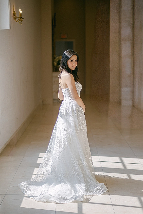 Bridal portrait of a bride in a strapless lace wedding dress with a long train, hair down, in a stone hallway with window light