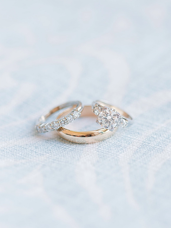 Wedding rings with a diamond engagement ring and matching diamond band stacked on light blue fabric with soft textured backdrop