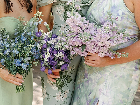 Bridesmaid bouquets with pastel bridesmaid bouquets in lavender and blue, hand-tied with wildflower stems, held on a sunlit outdoor walkway