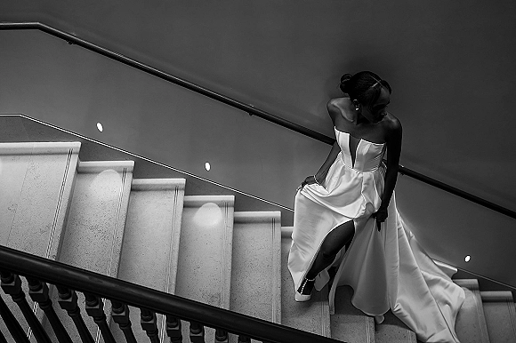 Bridal portrait in black and white of a bride on a staircase, looking over her shoulder in a strapless gown with thigh slit and long train