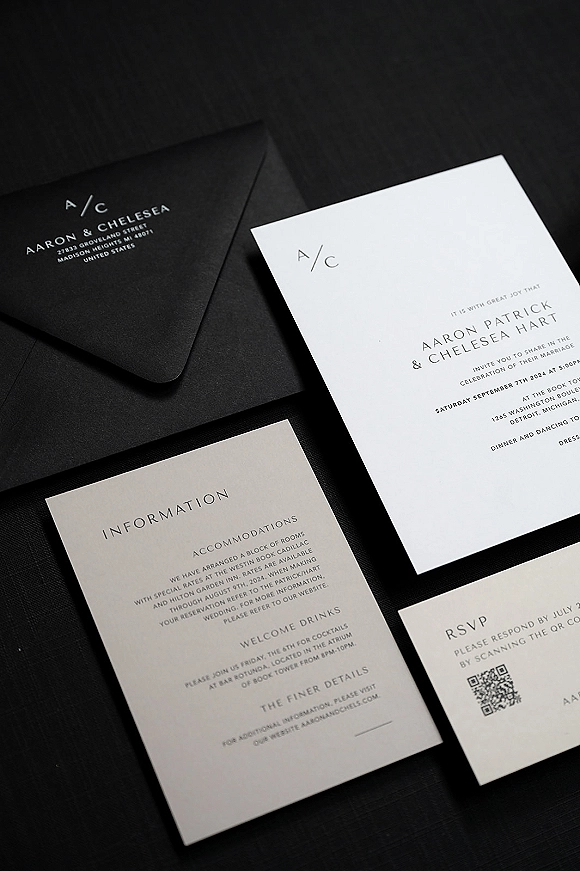 Wedding invitation suite with modern wedding invitations, including envelope, RSVP and details cards with a QR code on a black tabletop