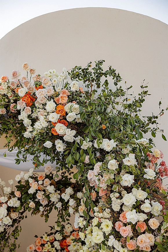 Wedding floral arch with ceremony floral arch roses and greenery vines draping an asymmetrical frame against a neutral indoor wall backdrop