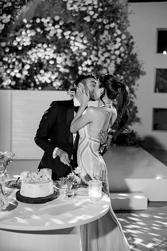 Wedding kiss as bride and groom lean over a candlelit cake table with buttercream wedding cake on an outdoor patio at night