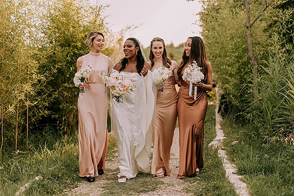 Bridesmaids portrait with bride and bridesmaids walking, holding white rose bouquets with ribbons along a bamboo-lined garden path