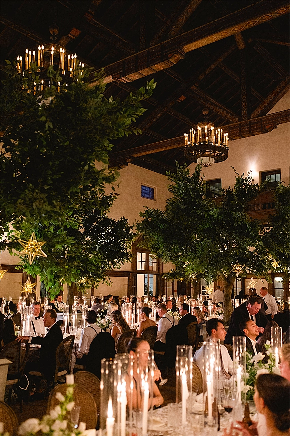 Reception decor with indoor reception lighting, hanging star lights over dining tables with tall glass candle cylinders in a ballroom with wood beams