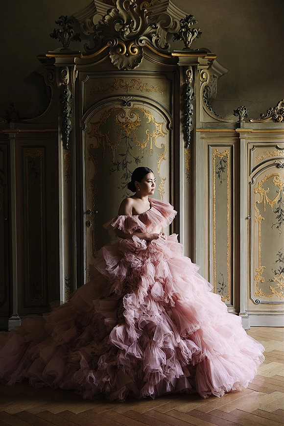 Bridal portrait of a bride in a blush pink wedding dress with off-the-shoulder tulle and long train against ornate gilded wall panels