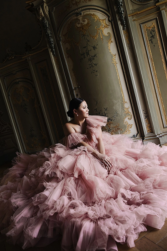 Bridal portrait in a pink tulle wedding dress with dramatic ruffles, seated on a wooden floor against ornate gilded paneled walls