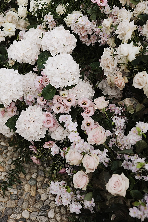 Wedding florals and white hydrangea arrangement with blush roses and greenery arranged low on a stone pebble ground walkway