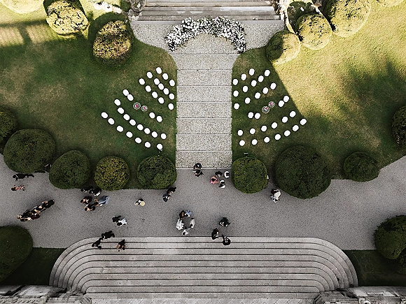 Outdoor ceremony setup with ceremony aisle layout, white chairs in a semicircle around a floral arch on a manicured lawn with stone steps