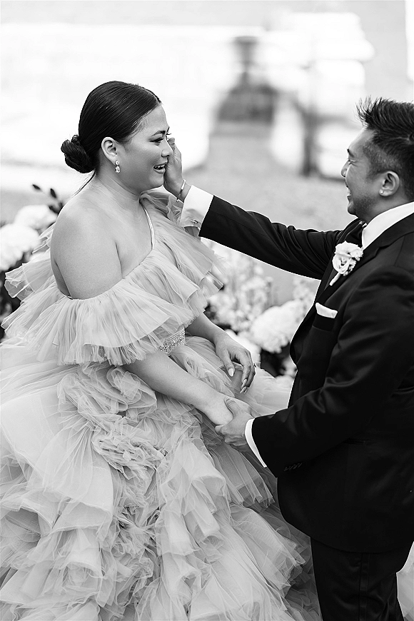 Wedding couple portrait of bride and groom holding hands as the groom wipes her tears, her ruffled tulle gown by a waterfront path