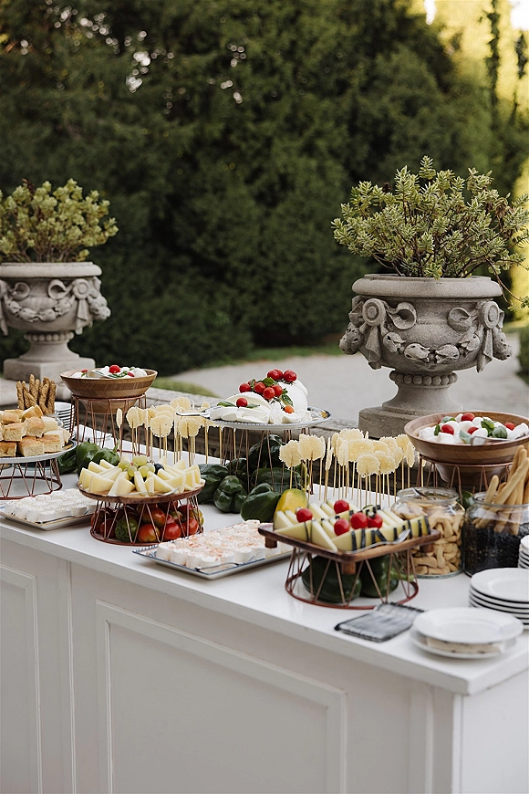 Wedding appetizer display with tiered serving stands of caprese skewers, cheese cubes, crackers, and breadsticks on an outdoor garden walkway