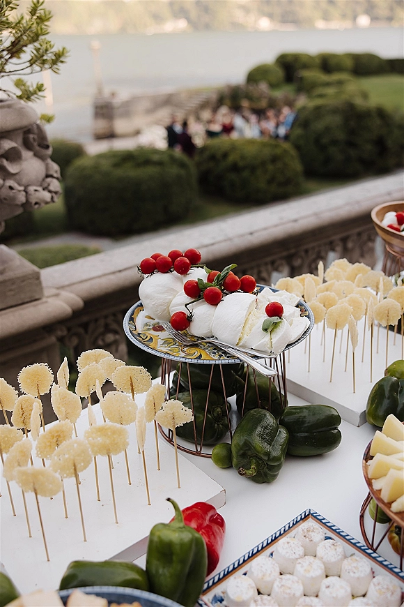 Wedding cocktail hour food on raised platters with caprese skewers, mozzarella, tomatoes and basil on a stone terrace by the waterfront