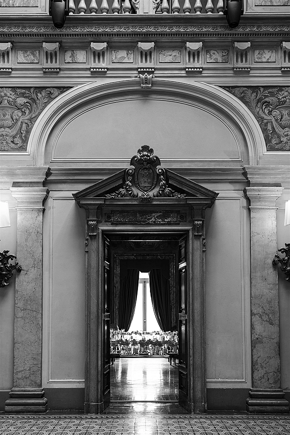 Reception room wedding reception hall with long banquet tables, crisp linens, glassware and floral centerpieces under draped curtains in a grand hall