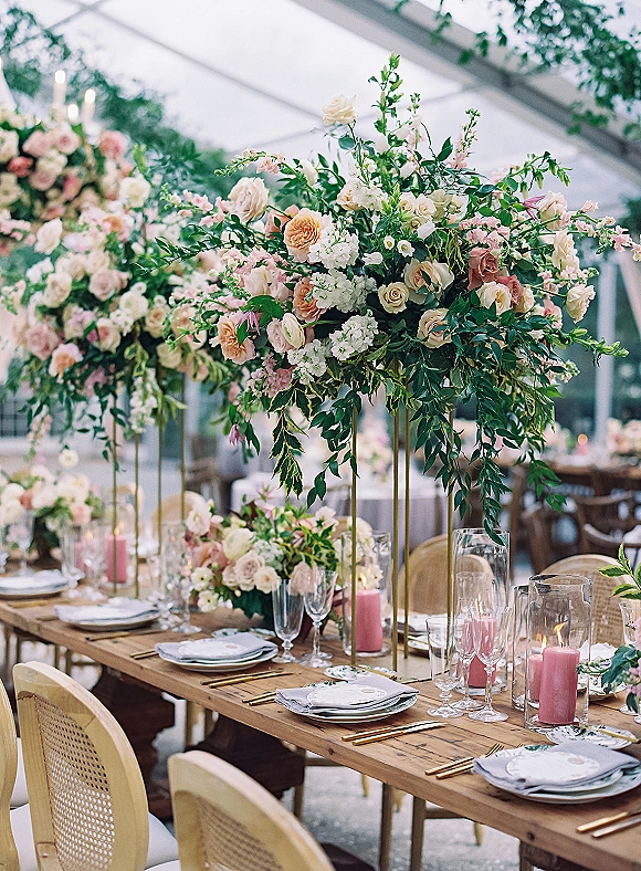 Reception tablescape with wedding reception table decor, tall rose and greenery centerpieces, pink taper candles, and gold flatware under a clear tent with string lights