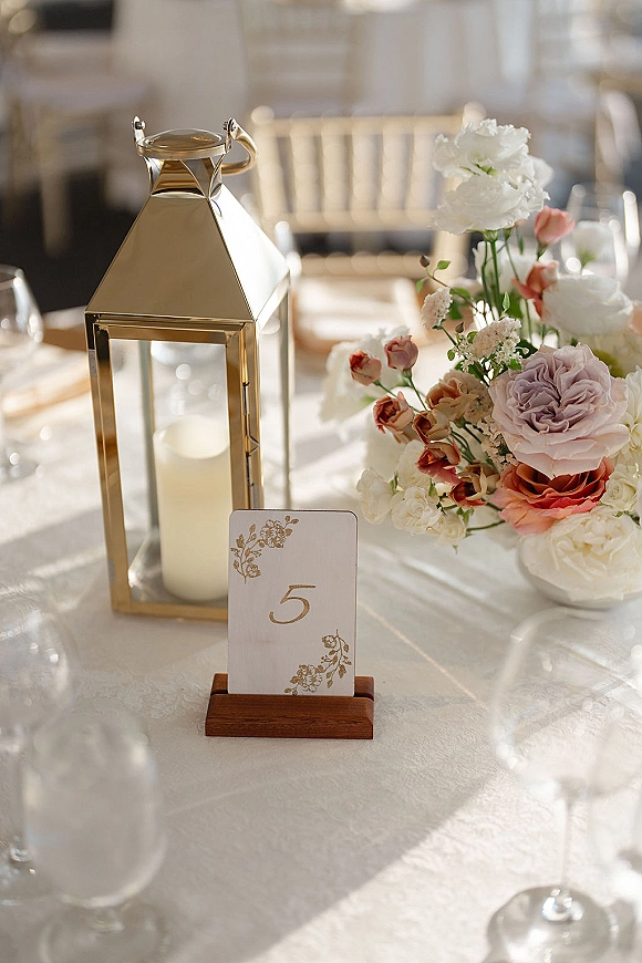 Wedding table centerpiece with a gold lantern centerpiece, pillar candle, and blush roses with hydrangea on a white reception table setting