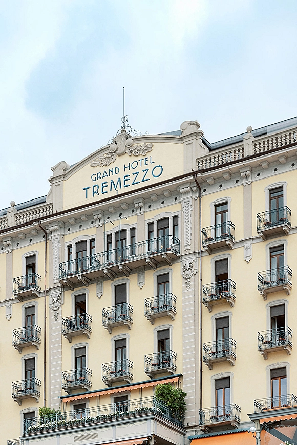 Hotel exterior with luxury hotel facade, wrought iron balconies, shuttered windows, and striped awnings beneath a clear sky
