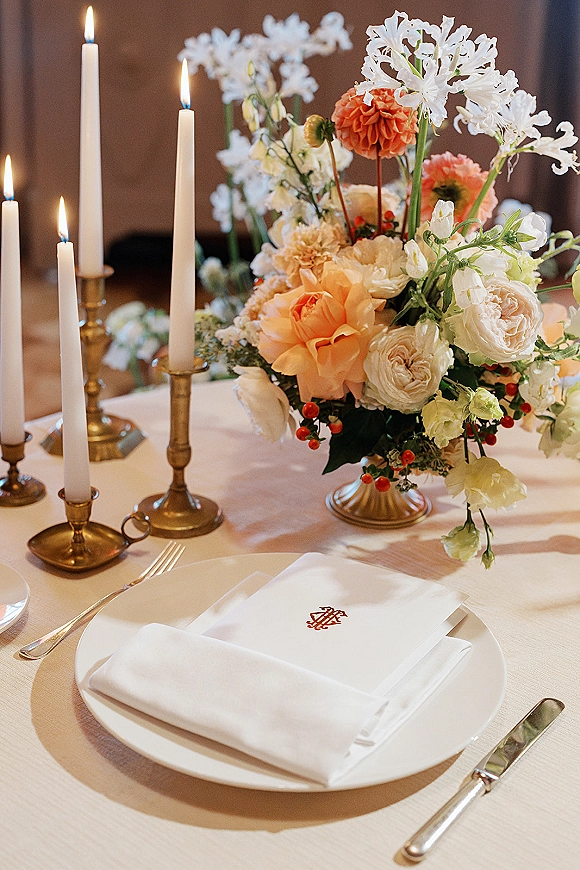 Reception tablescape with wedding table centerpiece of white and peach flowers, white taper candles in brass candlesticks on a banquet table