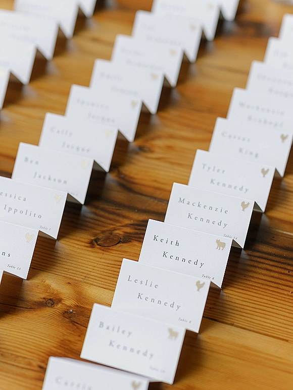 Wedding place cards with printed names and table numbers, folded tent style with gold animal icons arranged on a wood table