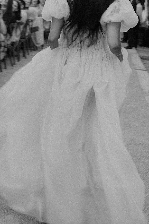 Wedding dress detail with puff sleeves and airy tulle skirt as the bride walks away on a stone walkway at an outdoor reception