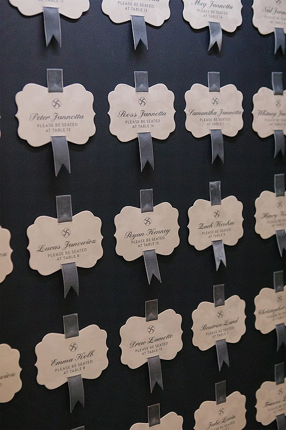 Escort card display with wedding escort cards featuring scalloped edges, printed calligraphy, and satin ribbon on a navy board, monogrammed