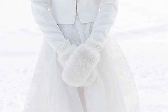 Bridal accessories with a wedding fur muff, white gloves and coat over a lace wedding dress in snowy outdoor winter light