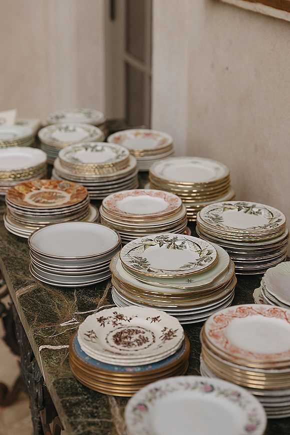 Wedding place settings with vintage china plates stacked with gold rim accents on a marble table near an indoor doorway