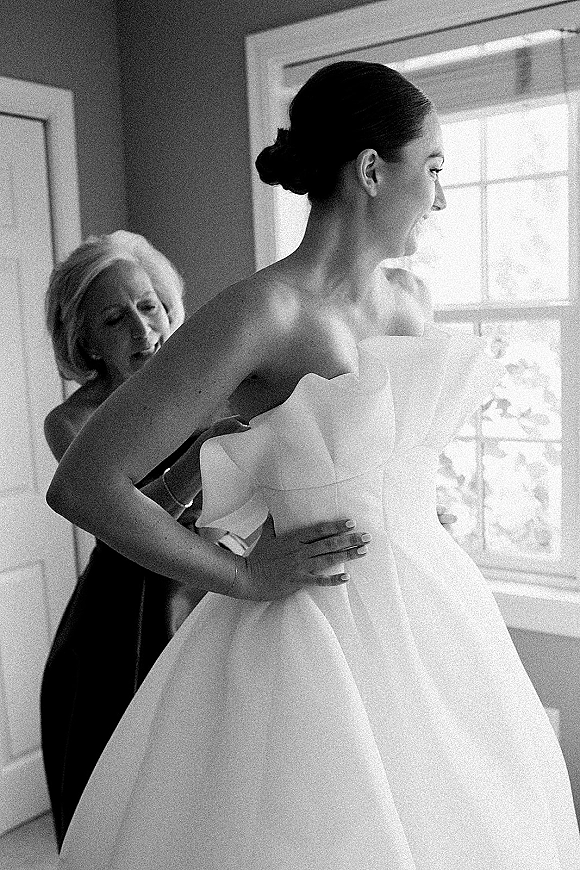 Bride getting ready in a strapless wedding dress fitting, low bun and bracelet, standing by window light in an interior room doorway