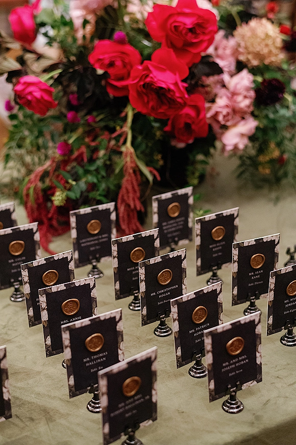 Wedding escort cards with wax seal escort cards arranged on stands on a tabletop, accented by a red rose and greenery centerpiece