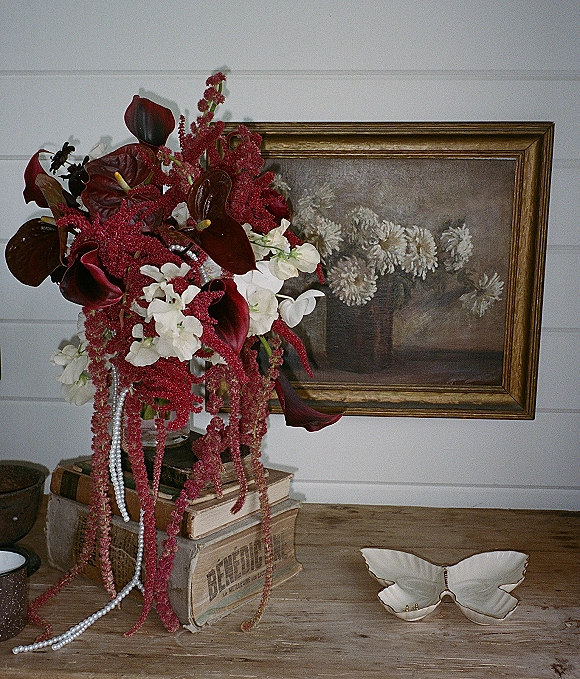 Bridal bouquet with burgundy calla lilies cascading red amaranthus, styled with a pearl strand on vintage books on a wood table