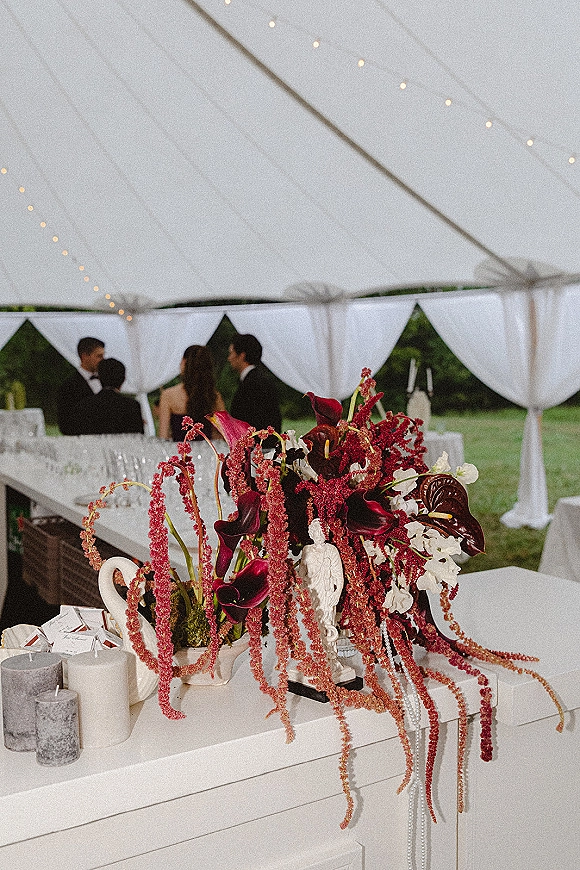 Wedding centerpiece with burgundy wedding centerpiece calla lilies, hanging amaranthus, candles, and pearl strands in a string-lit white tent reception