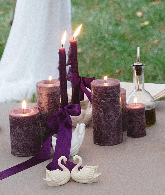 Wedding candle centerpiece with purple wedding candles, taper and pillar styles tied with ribbon and swan figurines on a lawn tablecloth