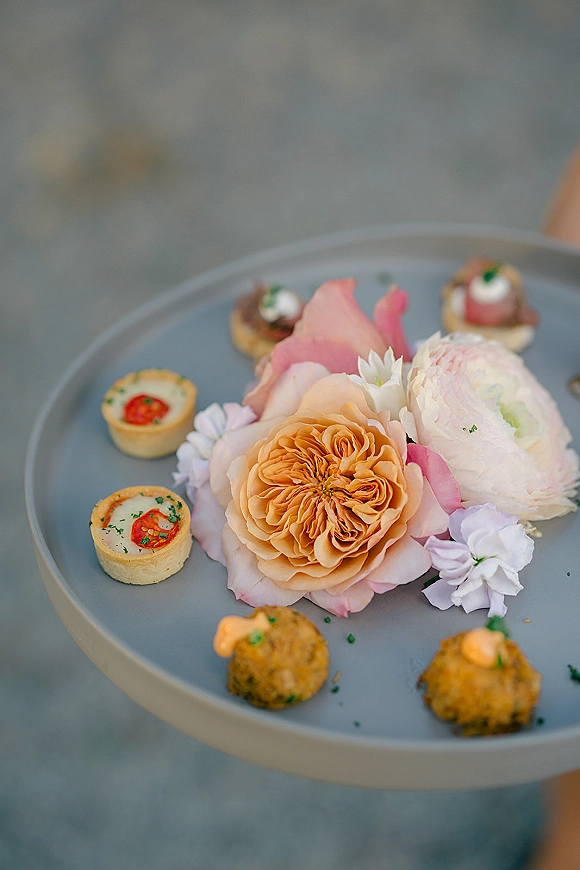 Wedding appetizers arranged as passed hors d'oeuvres on a gray stone surface, topped with edible flowers and microgreens on savory tartlets